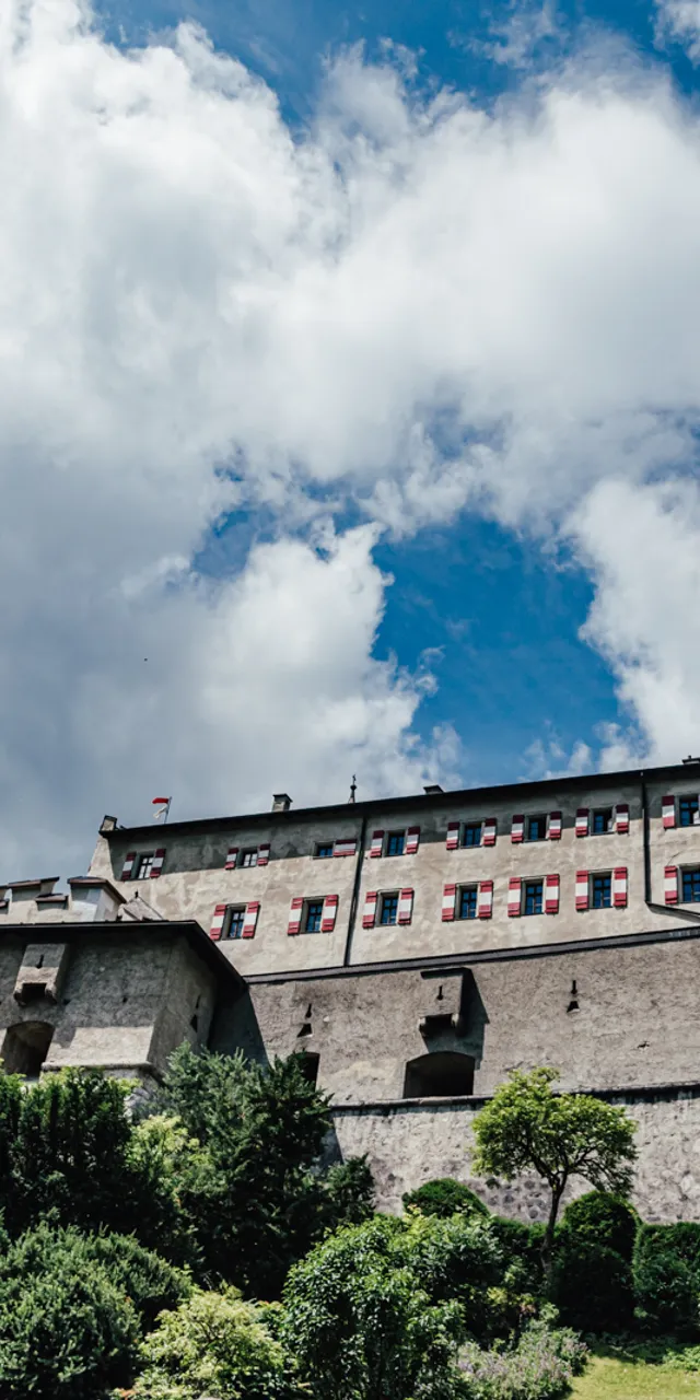 Historische Steinfestung mit roten Fensterläden und Türmen unter blauem, wolkigem Himmel
