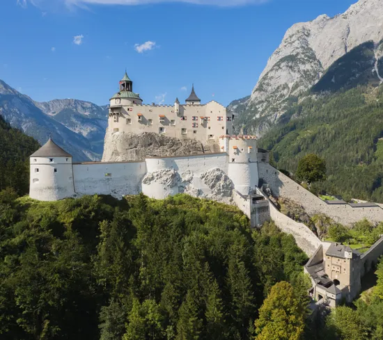 Historic Hohenwerfen Castle on a forested hill with Alps in the background