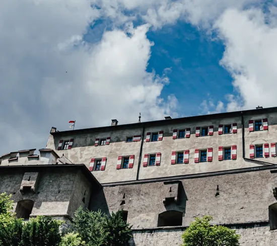 Historische Steinfestung mit roten Fensterläden und Türmen unter blauem, wolkigem Himmel