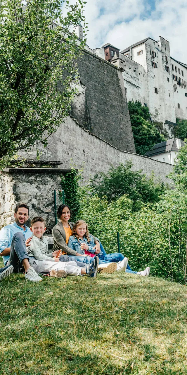 Family relaxing on hilltop near Hohenwerfen Castle surrounded by lush green trees