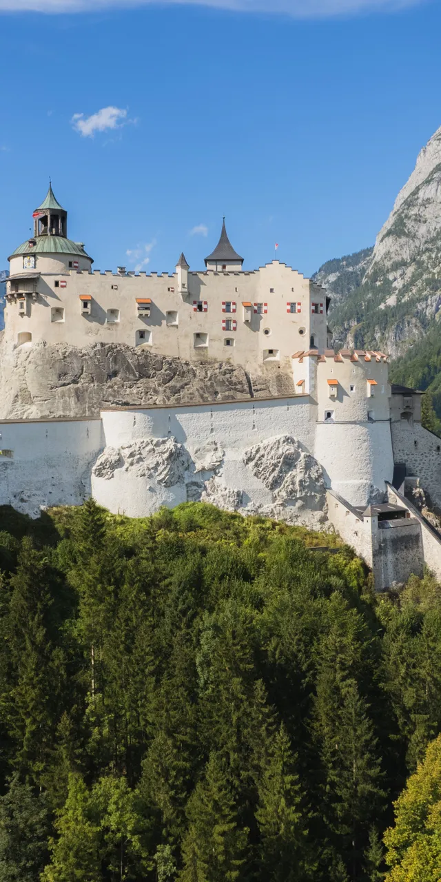 Historic Hohenwerfen Castle on a forested hill with Alps in the background
