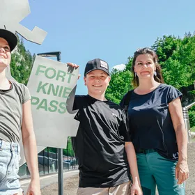 Lächelnde Familie mit Fort Kniepass-Schild am Eingang des Erlebnisparks an einem sonnigen Tag