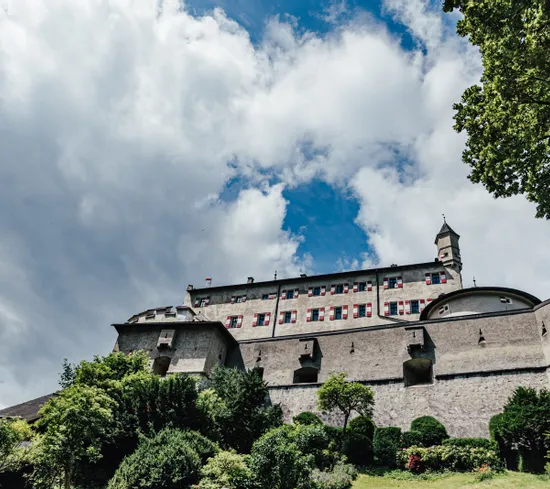 Historische Steinfestung mit roten Fensterläden und Türmen unter blauem, wolkigem Himmel